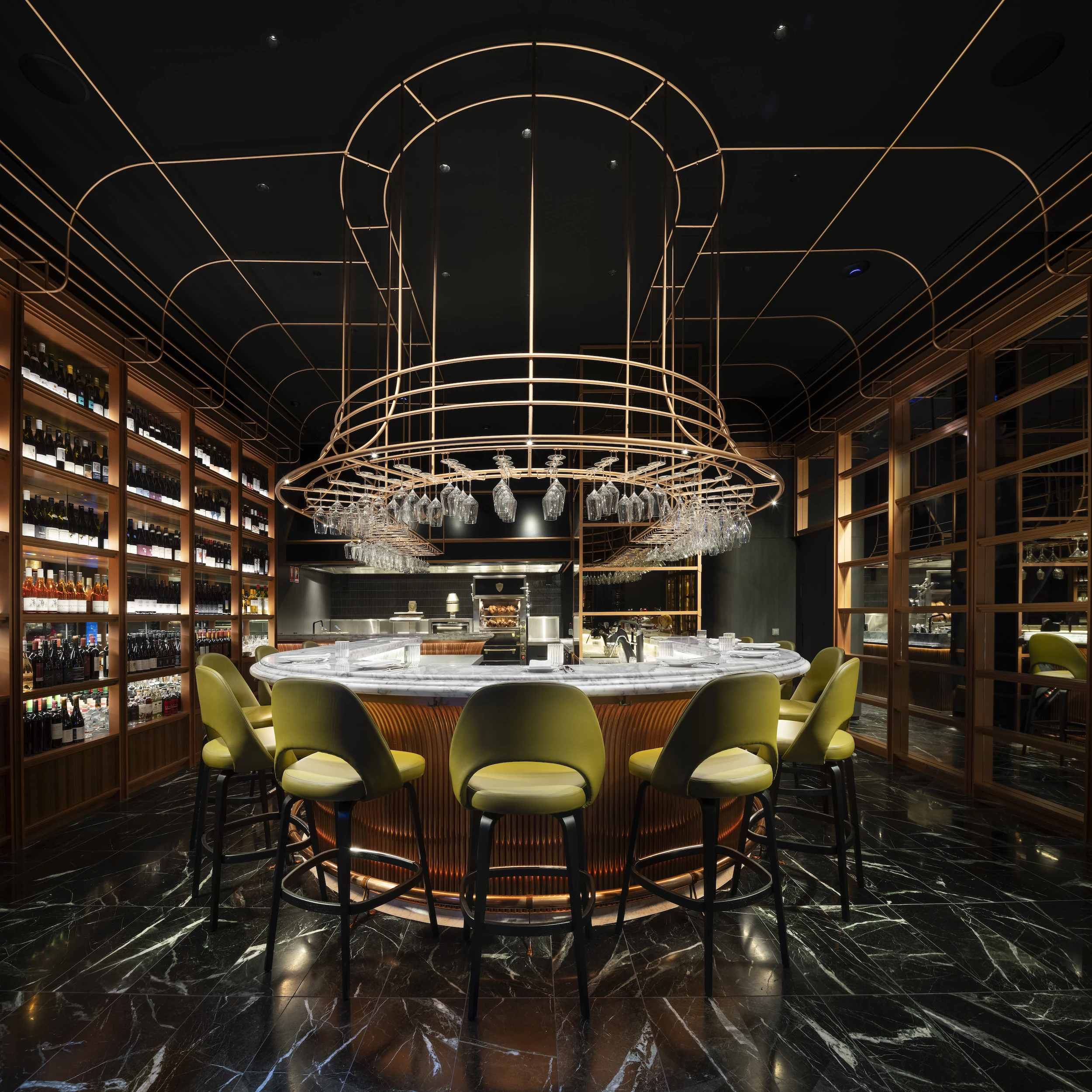 There is a round cocktail bar with green stools, and green marble floors, and wooden shelves running down the sides of the store