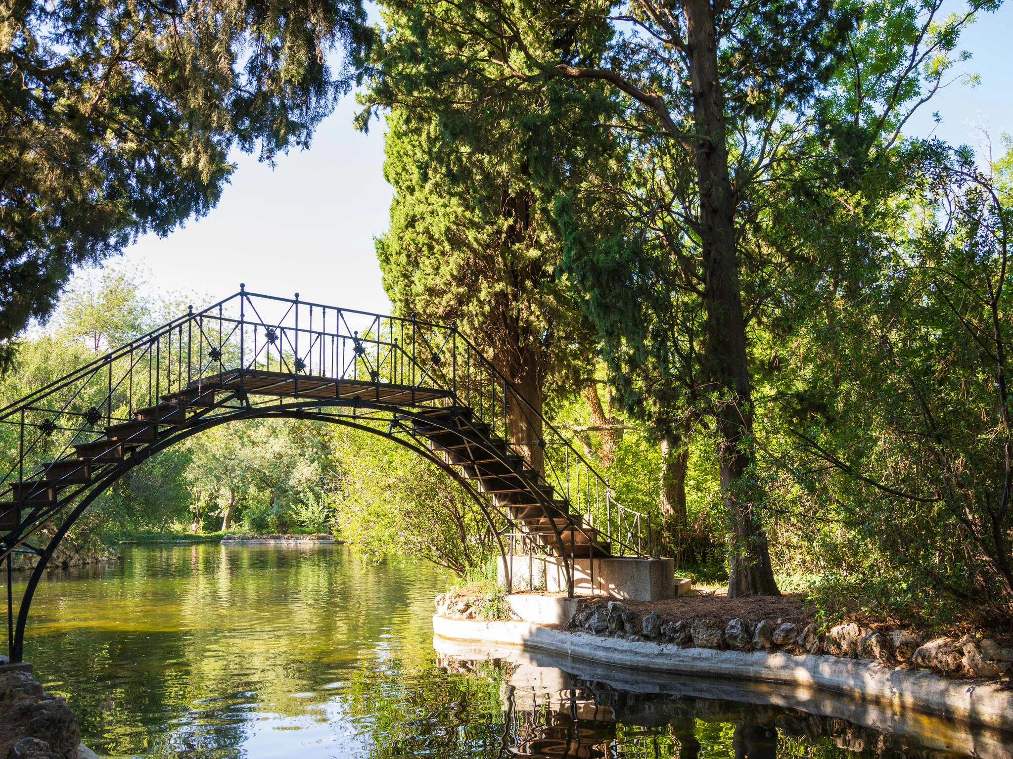 Horizontal view of a metal bridge over a pond with trees, in El Capricho park, in Madrid, Spain