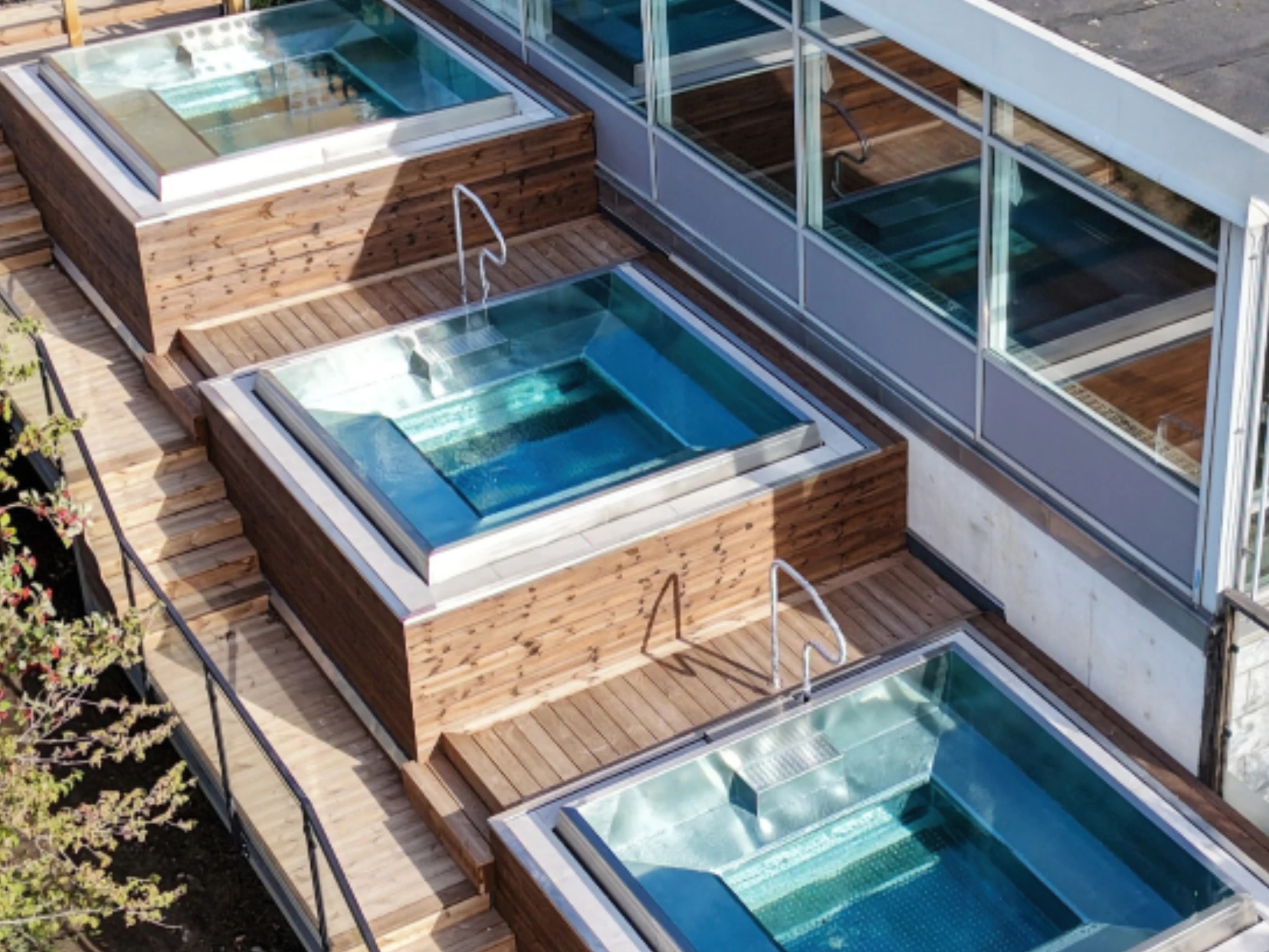 An aerial view of tiered wooden decks featuring multiple square outdoor hot tubs next to large windows at a spa in Lidingö.