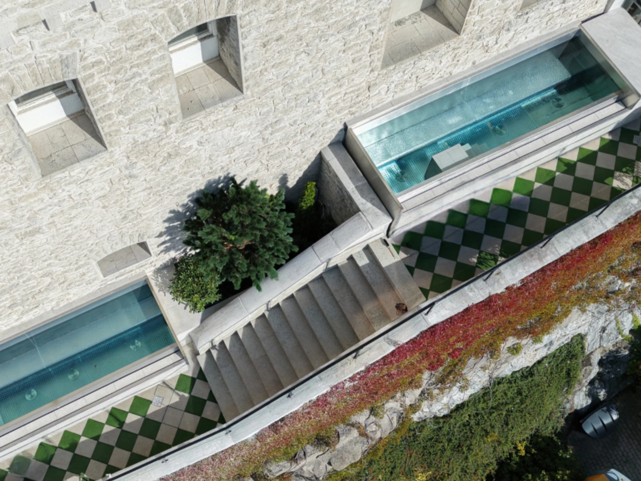 A high-angle aerial shot of a stone building terrace with geometric tiled walkways, stone steps, and narrow outdoor pools in Lidingö.