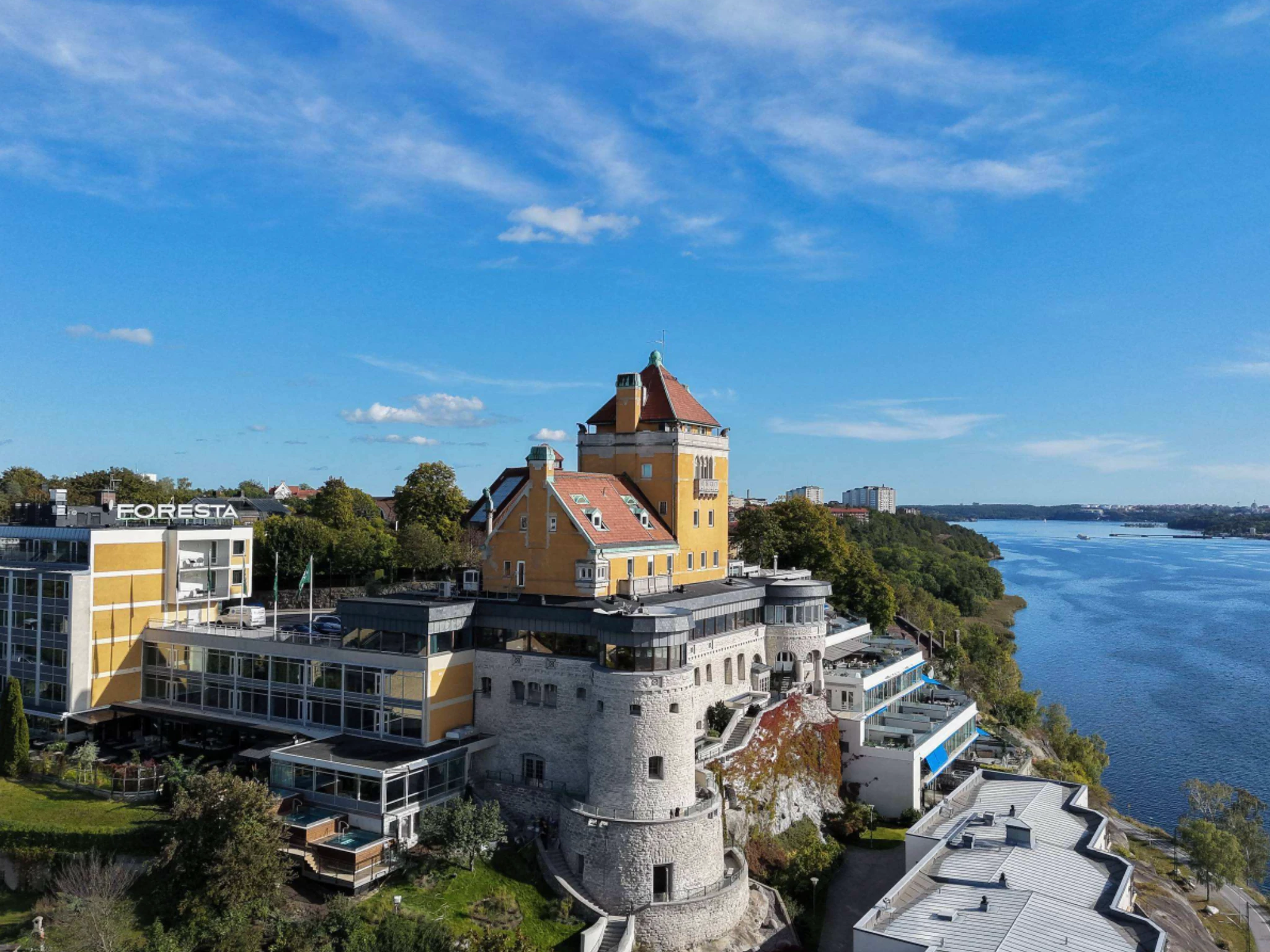 Panoramic aerial view of the historic Foresta castle hotel and spa perched on a cliff edge along the waterfront in Liding&ouml;, Stockholm.