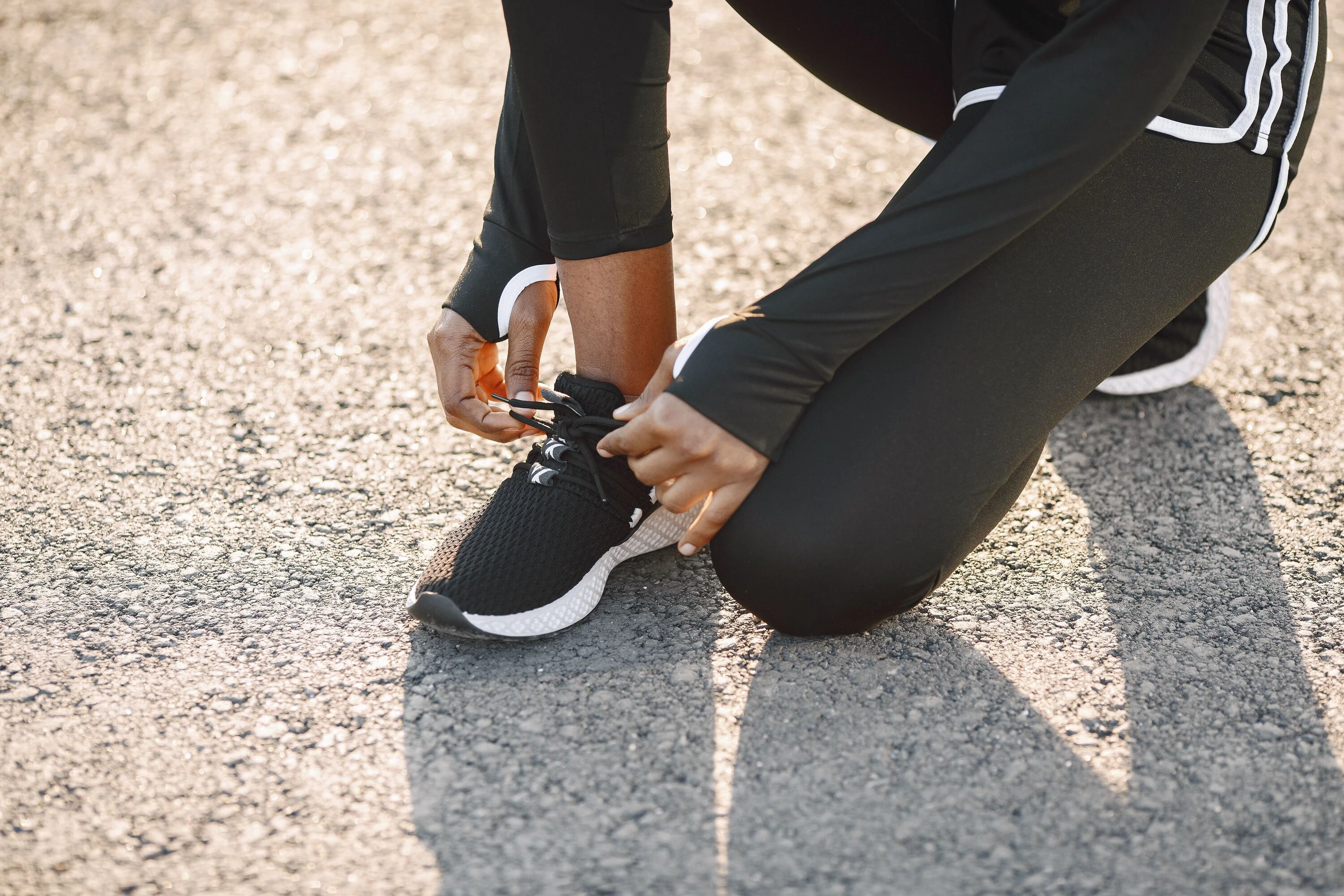 Close-up of a person tying black sports shoes on a sunny day, outdoors.
