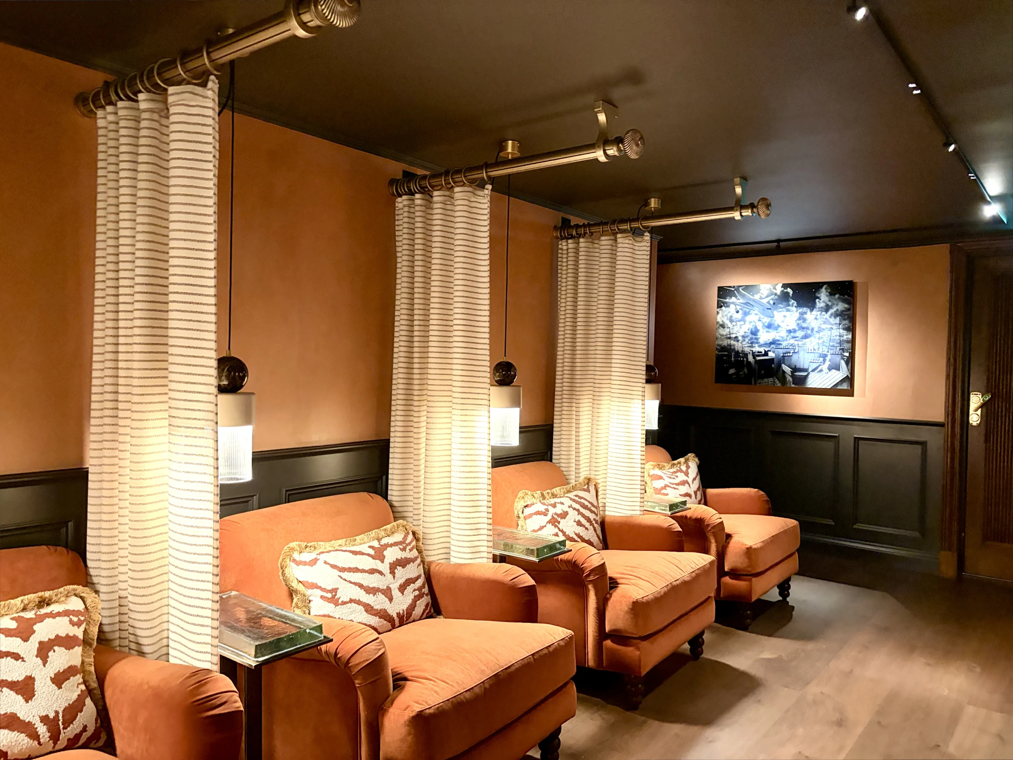 A row of comfortable plush orange armchairs separated by striped privacy curtains and lit by pendant lights in a warm, dark-toned spa relaxation lounge at Villa Foresta.