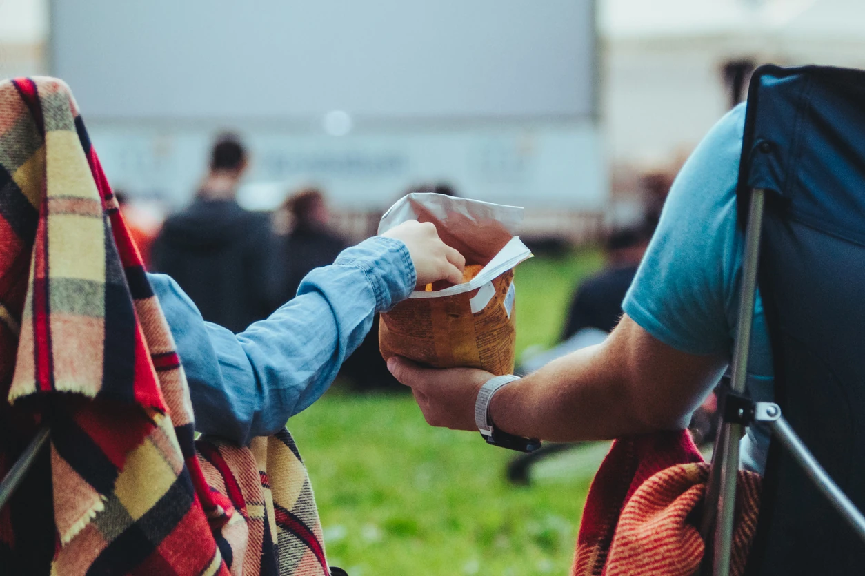 Couple sitting in camp-chairs in city park looking movie outdoors at open air cinema lifestyle