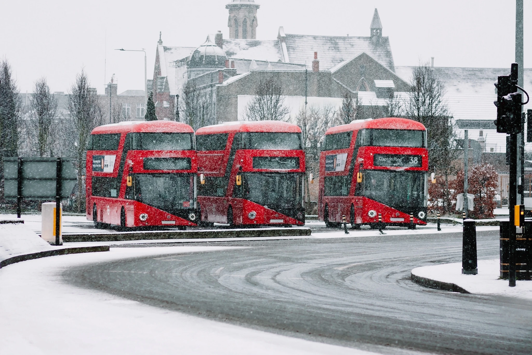 Three red London busses parked during a snow storm