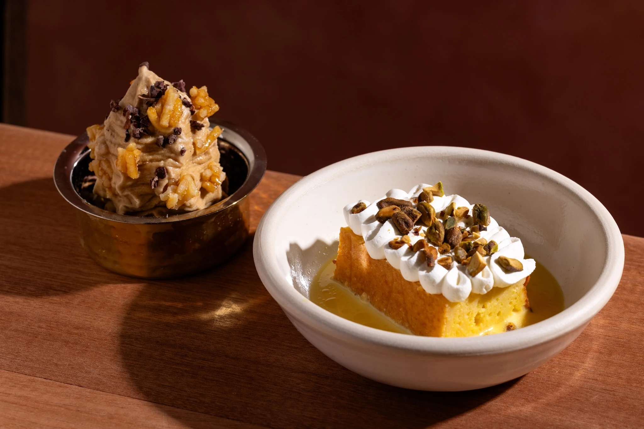 Ice cream in a metal bowl next to tres leche cake in a white bowl 