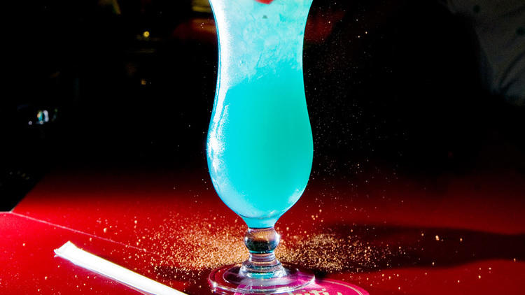 Blue Hawaii (Ingredientes: zumo de limón, piña, jarabe de azúcar, curaçao azul, ron, vodka, hielo picado en abundancia, rodaja de limón y la inevitable e imprescindible sombrilla.)