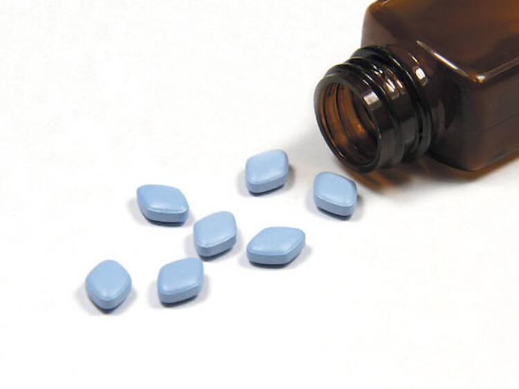 Blue anti-impotence tablets poured out from a bottle onto a white background