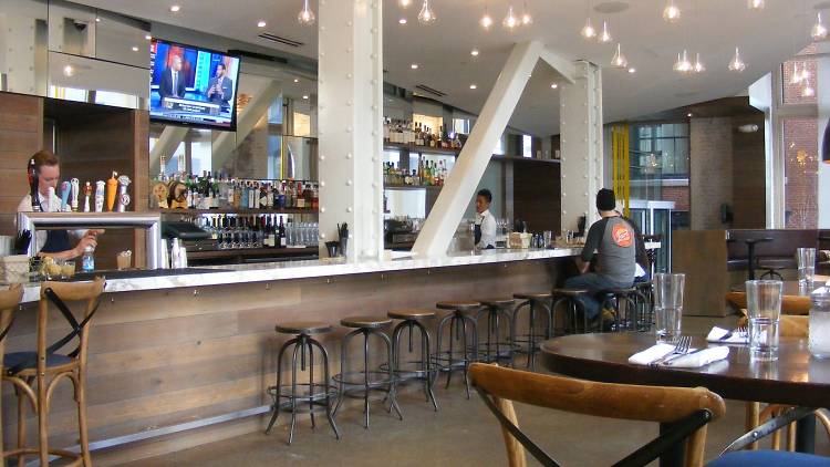 Inside Boston restaurant Trade, a patron sits at the bar while a bartender pours a beer