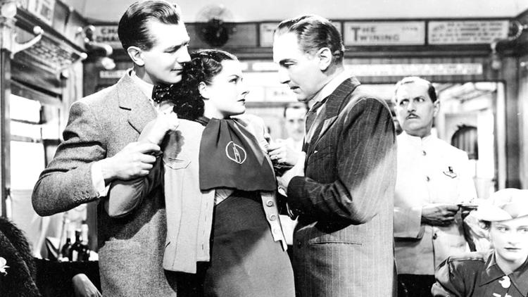 A still from the black and white film The Lady Vanishes of two men interrogating a women on a train