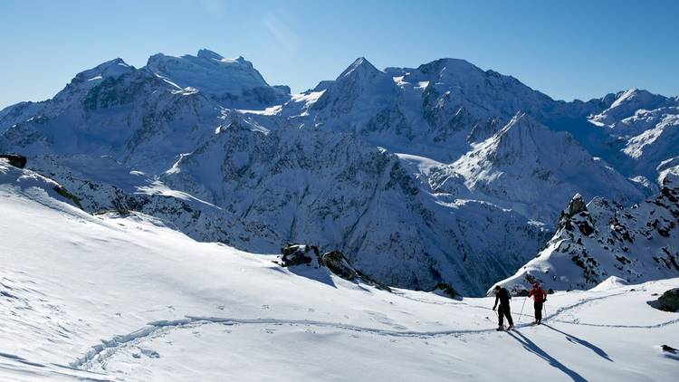 Two people walking up a snowy mountain on skis in Verbier.