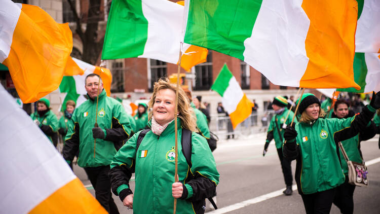 A woman marches in the St. Patrick's Day parade with Irish flags.