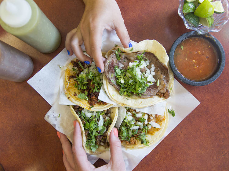 Two hands reaching for tacos on a platter.