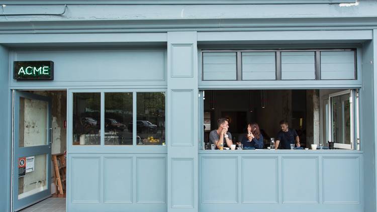 A shot of the front exterior of ACME with two diners sitting at