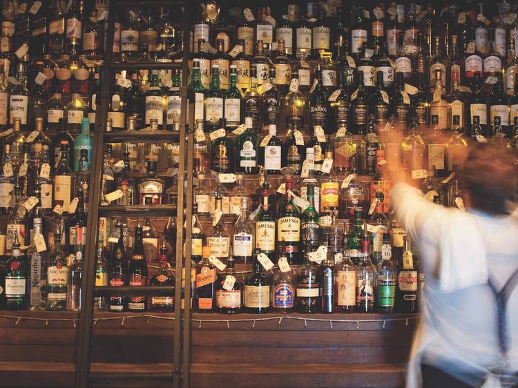 A bartender at Baxter Inn reaching up towards a large wall stack