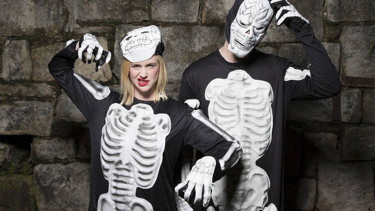 Two people standing up against a brick wall wearing skeleton hal