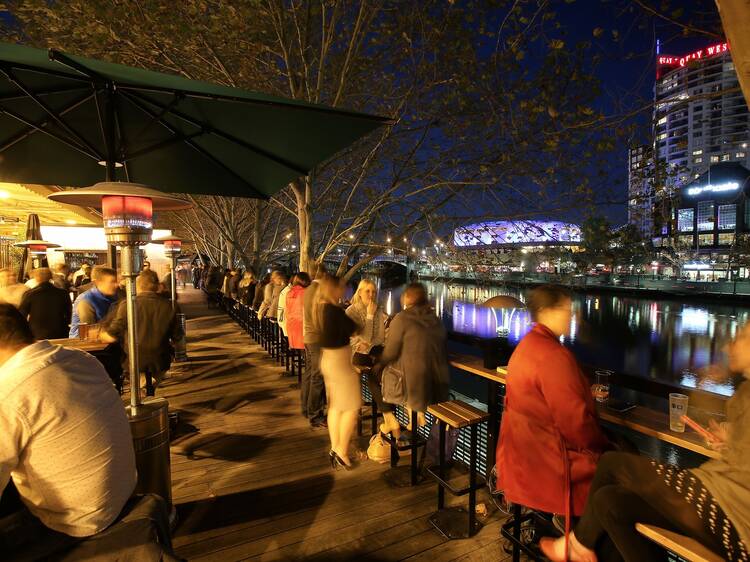 A shot of the outdoor area with people sitting on stools drinkin