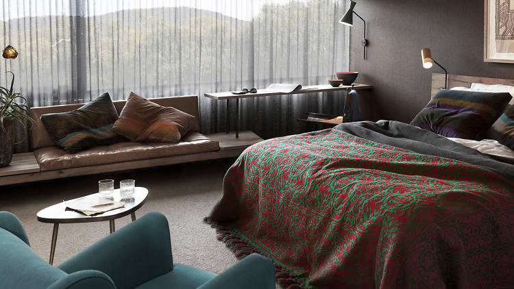 A shot of a guest room with a bed, couch and a large window overlooking trees and mountains
