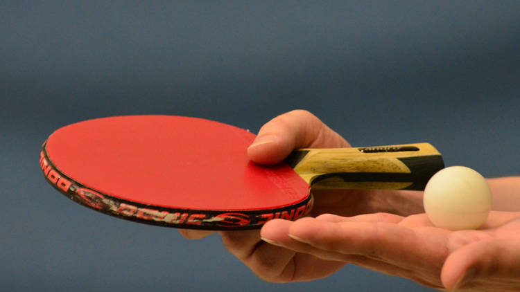 A close up shot of a table tennis paddle and ball being held in