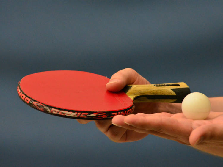 A close up shot of a table tennis paddle and ball being held in