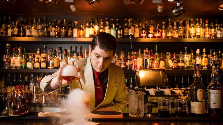 A bartender behind the bar at Eau De Vie pouring a steaming cock