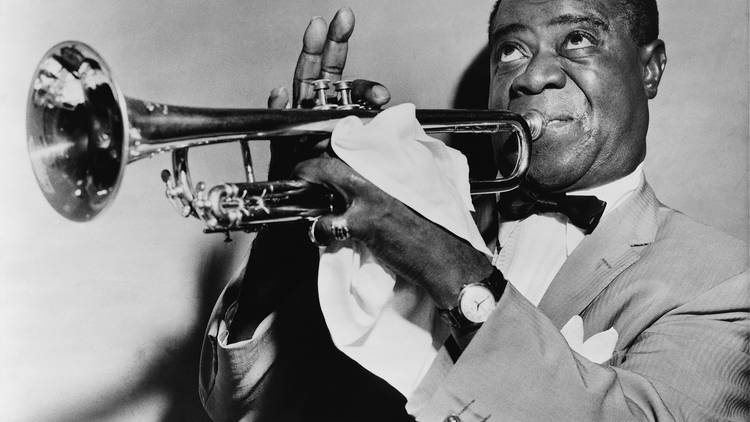 A black and white photograph of Louis Armstrong playing a trumpet