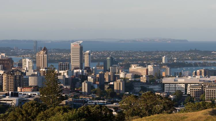 A photograph of the Auckland skyline, facing towards the city's harbour, with olive green hills in the foreground