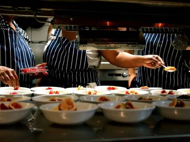The pass at Mazi Mas Chefs plating up dessert behind a kitchen pass