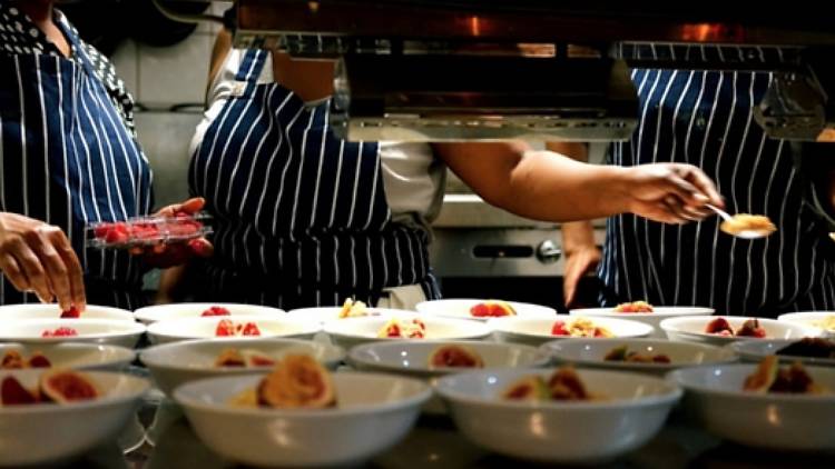 Chefs plating up dessert behind a kitchen pass