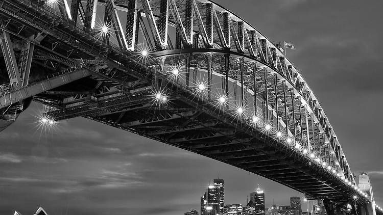 A black and white photograph of the Sydney Harbour bridge, taken at night with the lights on.