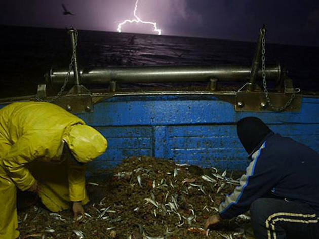 Lampedusa in Winter Two men on a fishing boat at nighttime while lightning appears in the distance