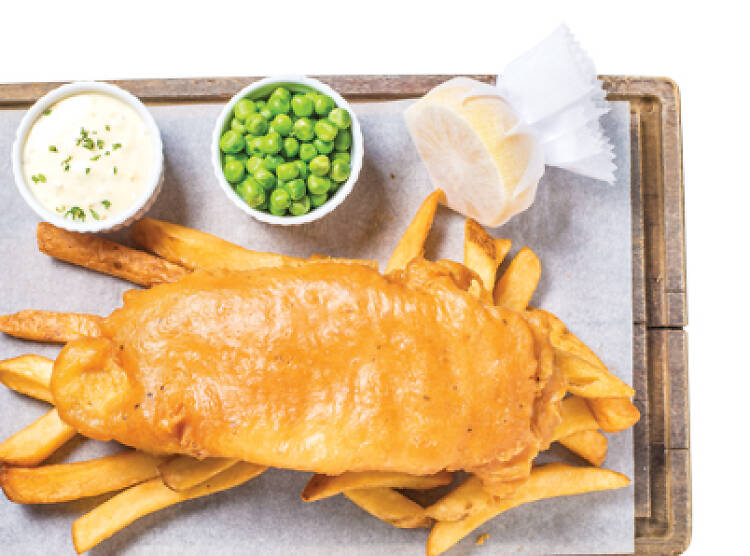 a plate of fish and chips with lemon, tartare sauce and peas