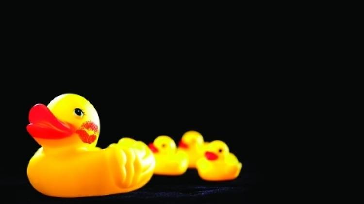 A row of rubber ducks, the front one has a lipstick stain