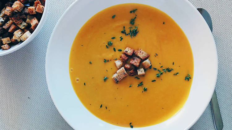 A bowl of orange-coloured soup with croutons on top