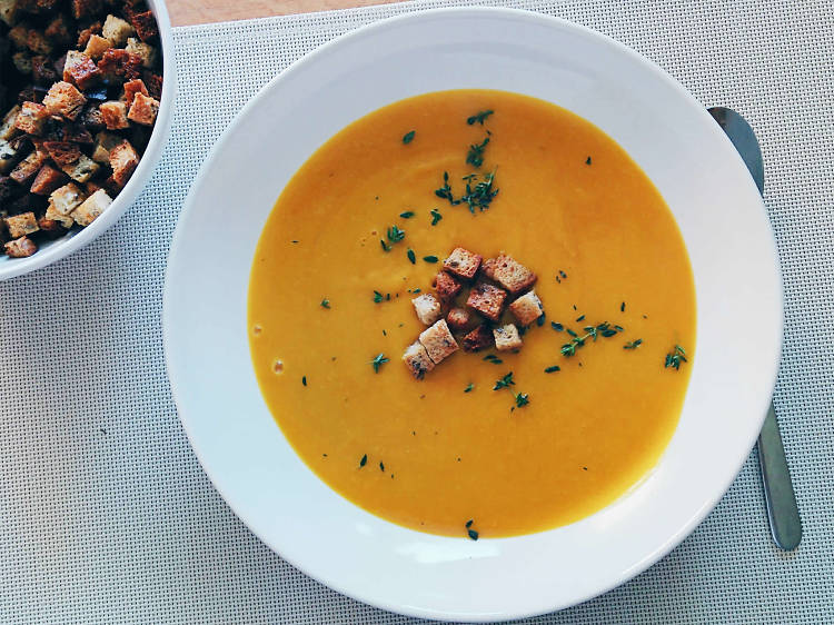 A bowl of orange-coloured soup with croutons on top