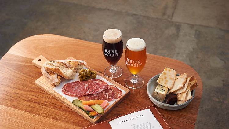 Two beers on a wooden table with a charcuterie platter