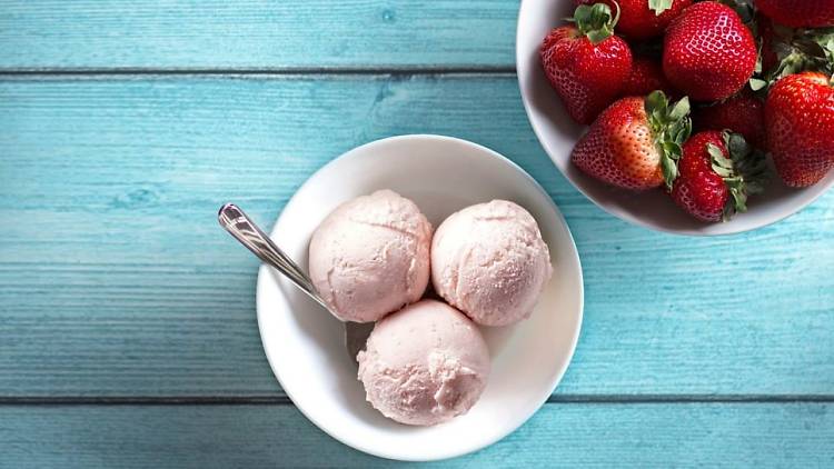 Bowl of strawberry ice cream next to a bowl of strawberries