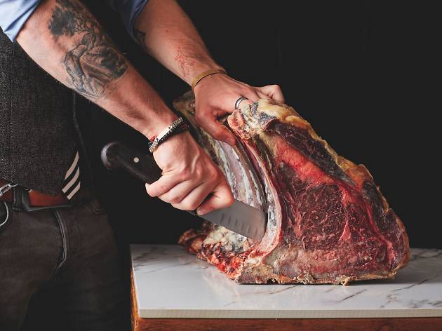 Blue Butcher with tattooed arms cutting meat