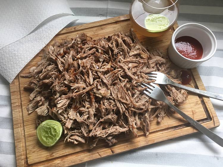 A try full of pulled pork with sauce, lime and a jug of cocktails in view