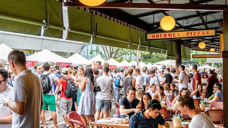 A group of people drinking and eating at tables under an awning