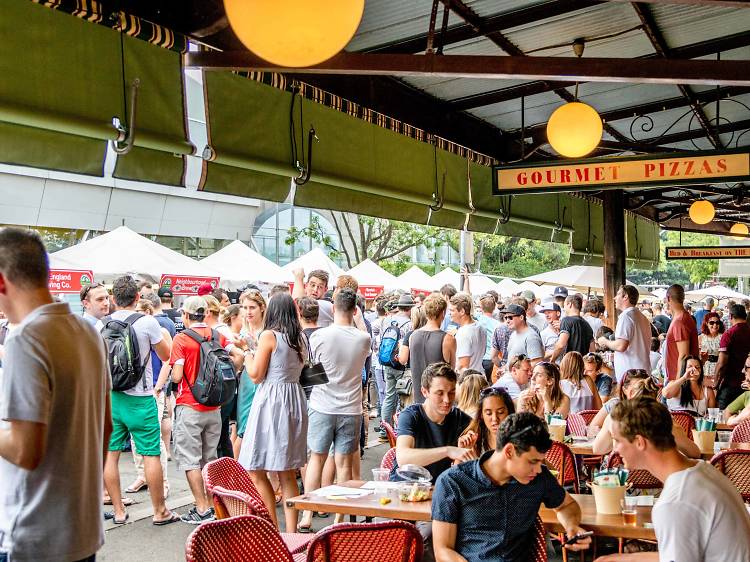 A group of people drinking and eating at tables under an awning