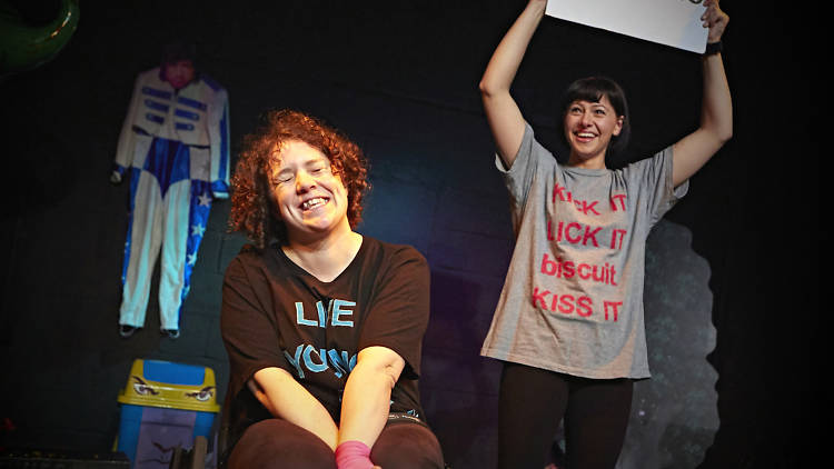 Two women, one sitting in a wheelchair, the other standing and holding a sign which reads 'Swearing'