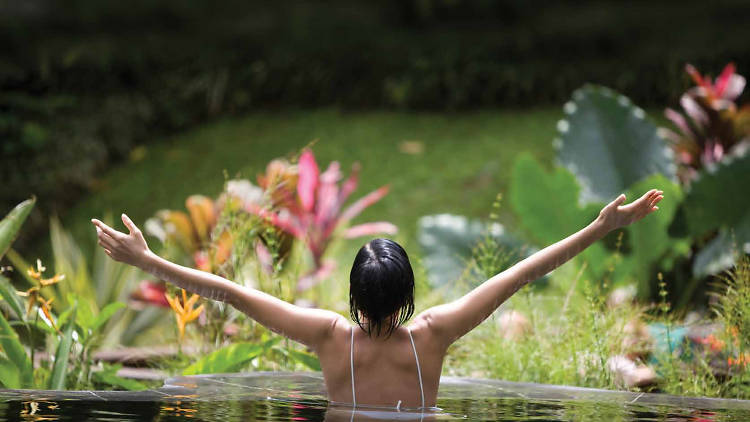 A woman stretches out her hands in a pool of water surrounded by greenery at Jindii Eco Spa