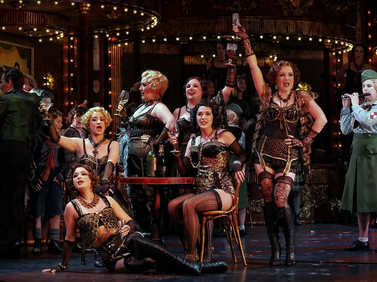 Women sit at a table drinking champaign in flapper-style lingerie on the set of La Boheme