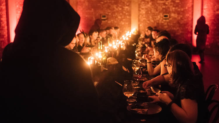 Cloaked figures around a candlelit table