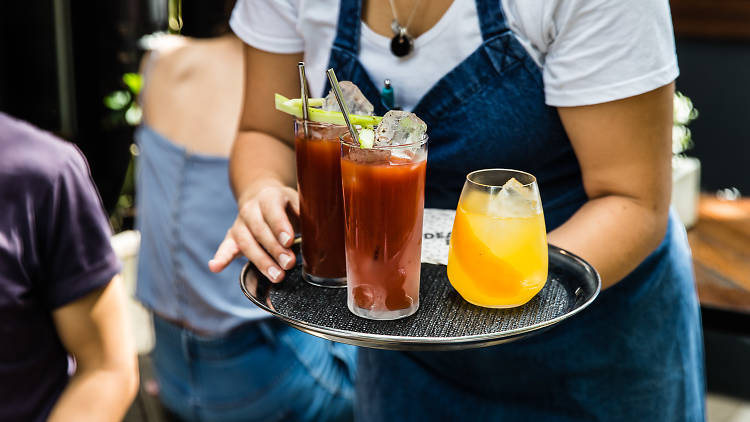 A waiter carries of tray of Bloody Mary and Mimosa cocktails during brunch at Surry Hills bar Dead Ringer