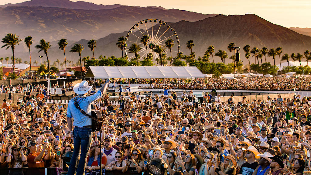 A country singer holding a guitar points out at a packed audience below.