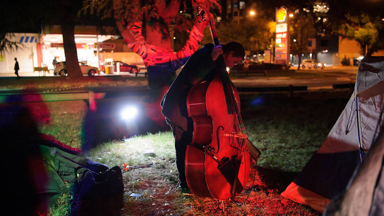 A cellist plays on a grassy lawn at night, lit in red light