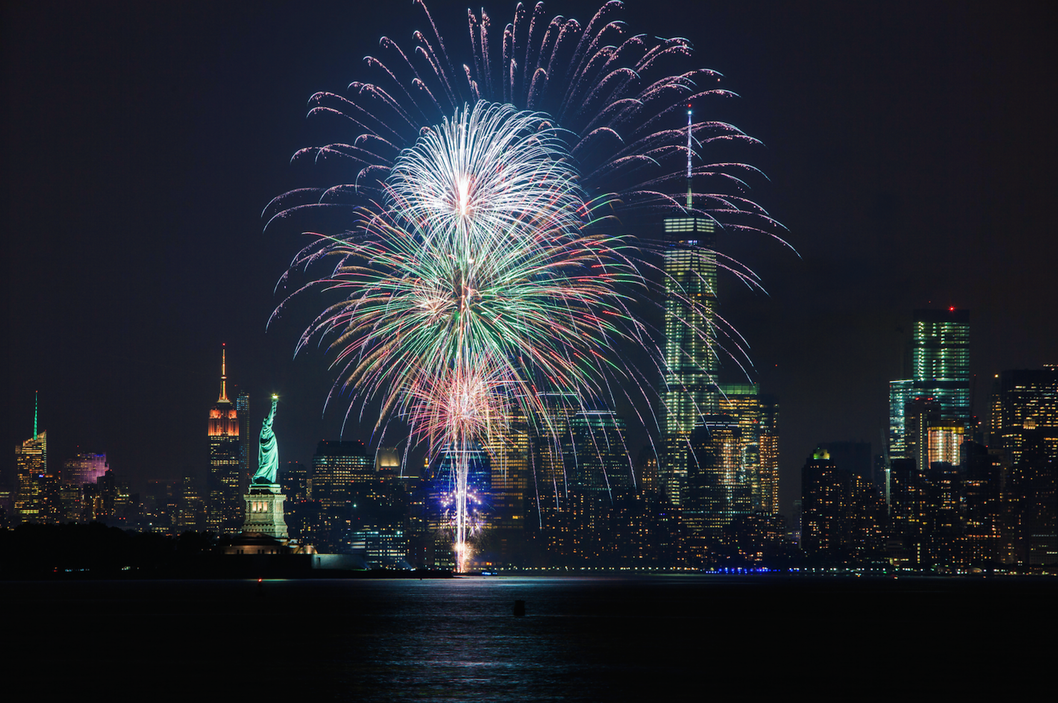 Photo of large colorful fireworks lighting up the sky above downtown Manhattan and the Statue of Liberty