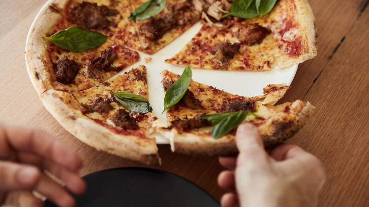 Person taking a slice of woodfired pizza